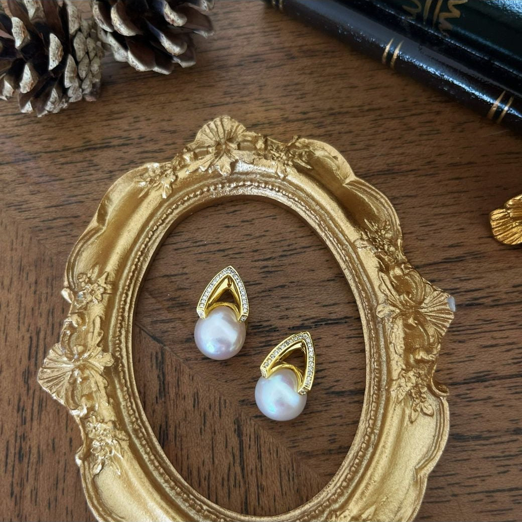 Arché gold white pearl earrings styled inside an ornate gold frame