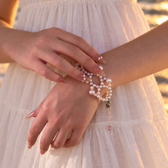 Ballet Rosé pink pearl weave bracelet worn with a white dress, showing the adjustable extender