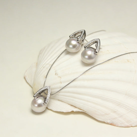 Arché silver grey pearl earrings and pendant beside a spiral shell on black