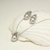 Arché silver grey pearl earrings and pendant beside a spiral shell on black